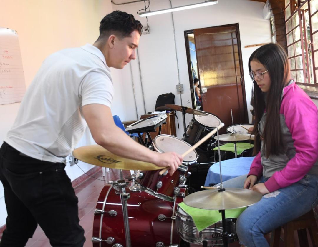 Tallerista enseñandole a estudiante a tocar la bateria 